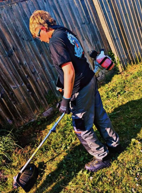 a teenage boy cutsgrass with a strimmer