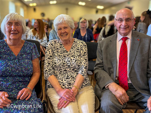 two men and a woman sat in a school hall smile for photo