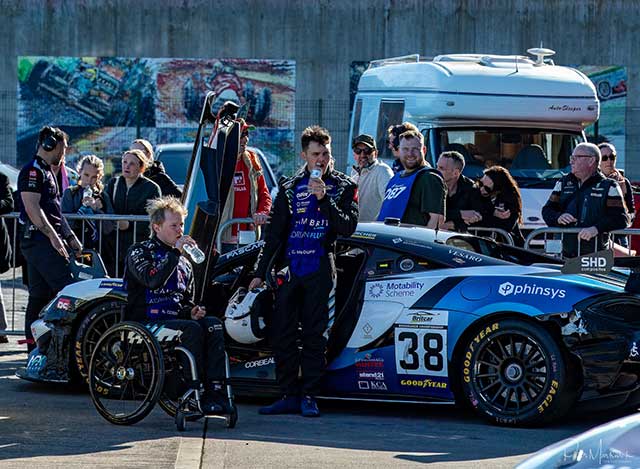 a racing car with the driver stood by door and other nearby