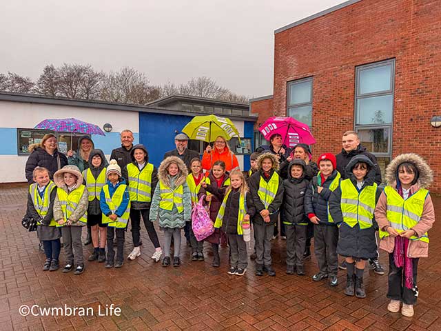 a group of pupils and staff stood outside a school in the rain