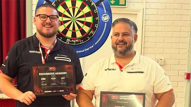 two men hold certificates in front of a darts board