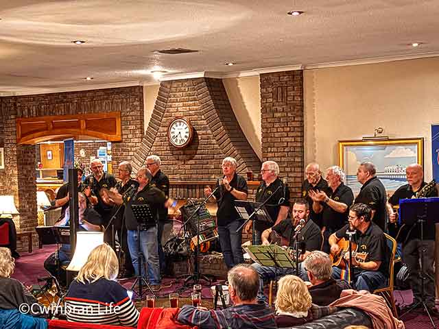 a sea shanty band perform in a hotel lounge to a crowd of people