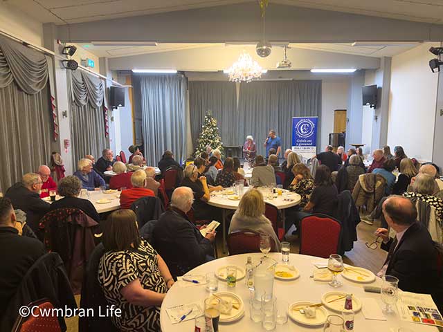 a room full of people sat at tables looking towards a woman at the front of the room