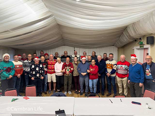 a large group of men and some women standing and smiling at camera- many in christmas jumpers