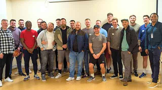 a group of about 25 men stood smiling for a photo in a group