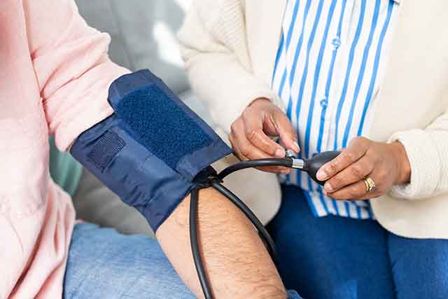 Measuring blood pressure, healthcare worker checking senior patient's arm at home