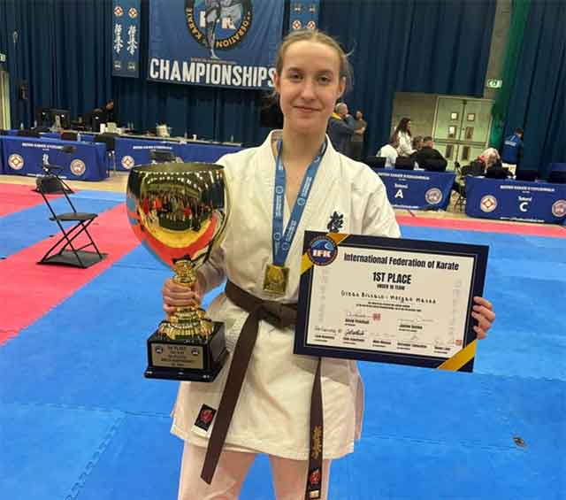 a woman holding a trophy she won in karate tournament. She's stood on the mats