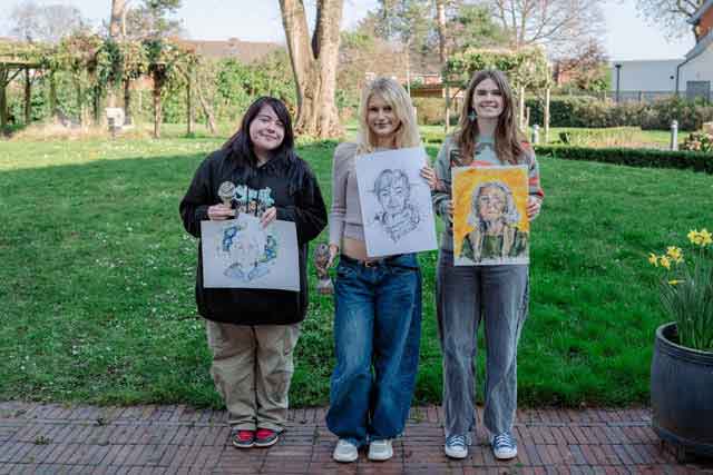 three women holding portraits they've drawn of older people