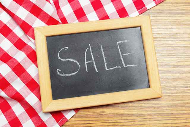 A framed chalkboard with the word "SALE" written in chalk is on a wooden table next to a red and white checkered cloth.