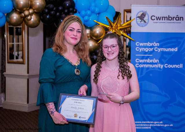 two women hold a certificate in front of a balloon arch