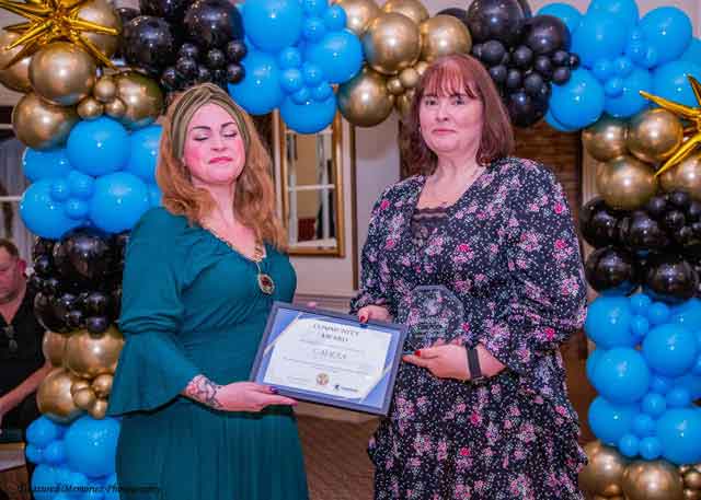 two women hold a certificate in front of a balloon arch