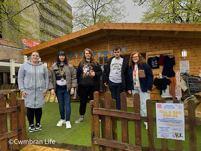 a group of students and a tutor by a log cabin in a town centre