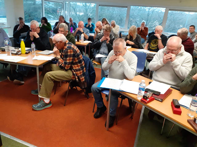 a room of people sat at desks holding harmonicas