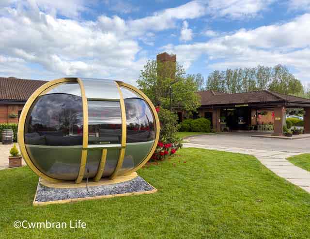 a glass garden pod on a lawn outside a hotel