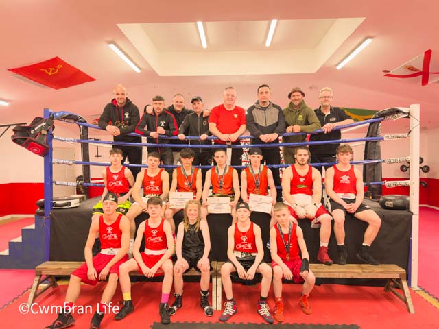 a large group of boys and men sit and stand by a boxing ring