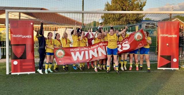 a women's football team celebrate holding up a trophy