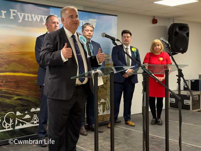 a man gives a speech at a lecturn with four people in the background