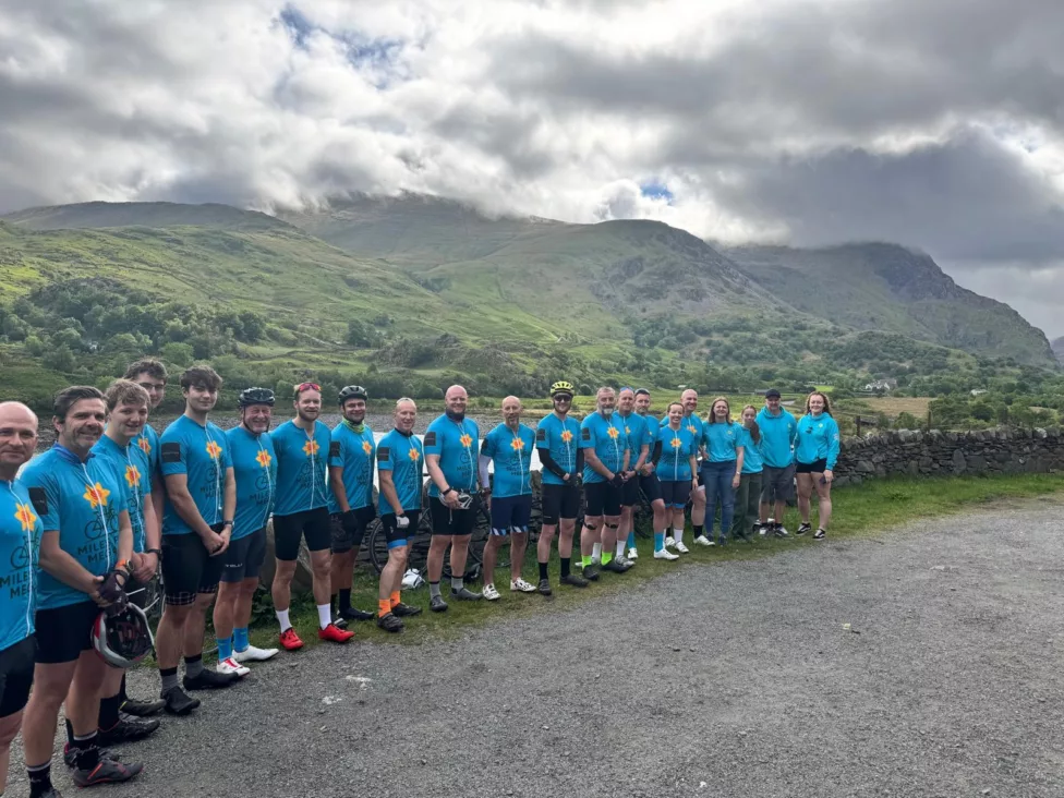 a group of 30 cyclists in a mountain area smile at the camera