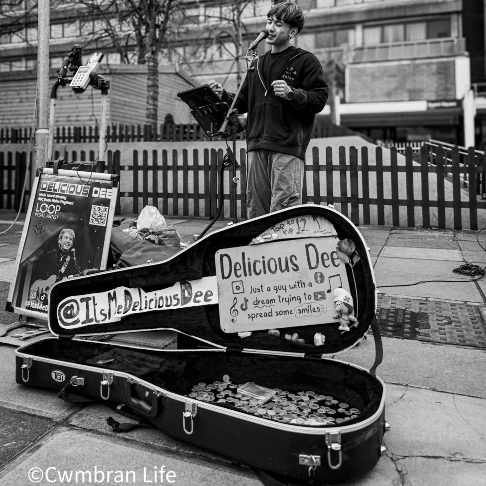 a black and white photo of a man singing and playing a guitar - he's busking in a town centre