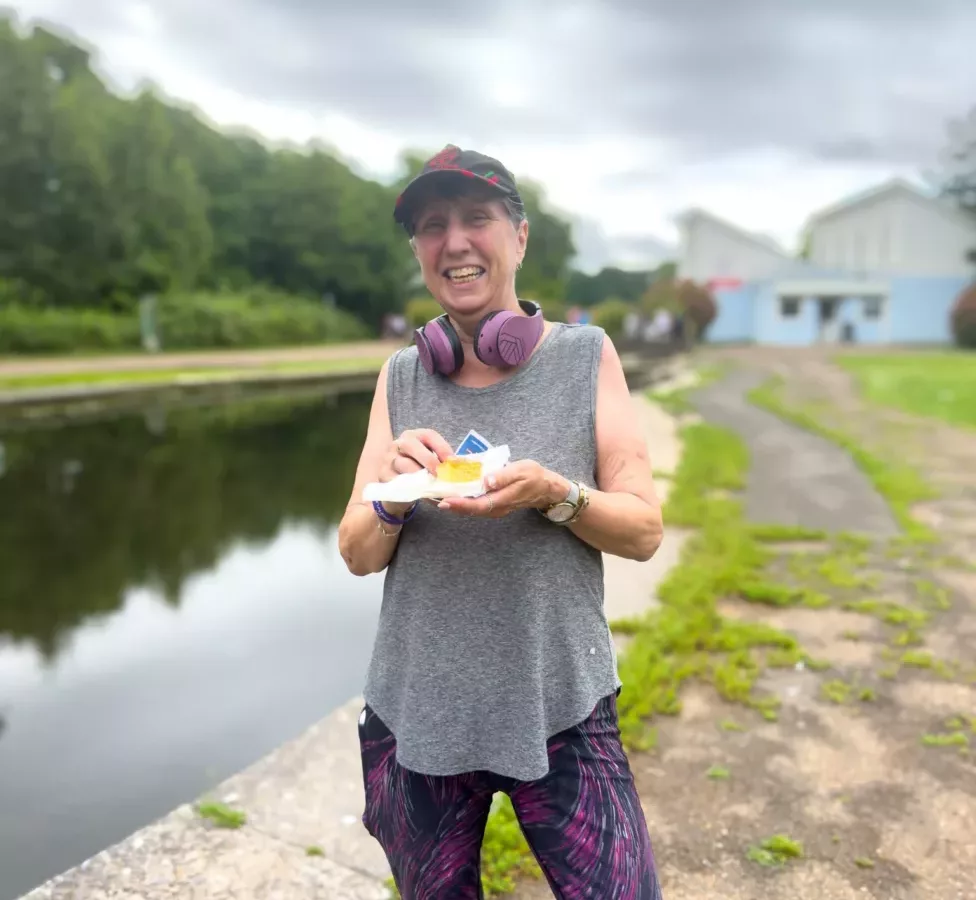 a woman in running clothes eating a cake by a pond