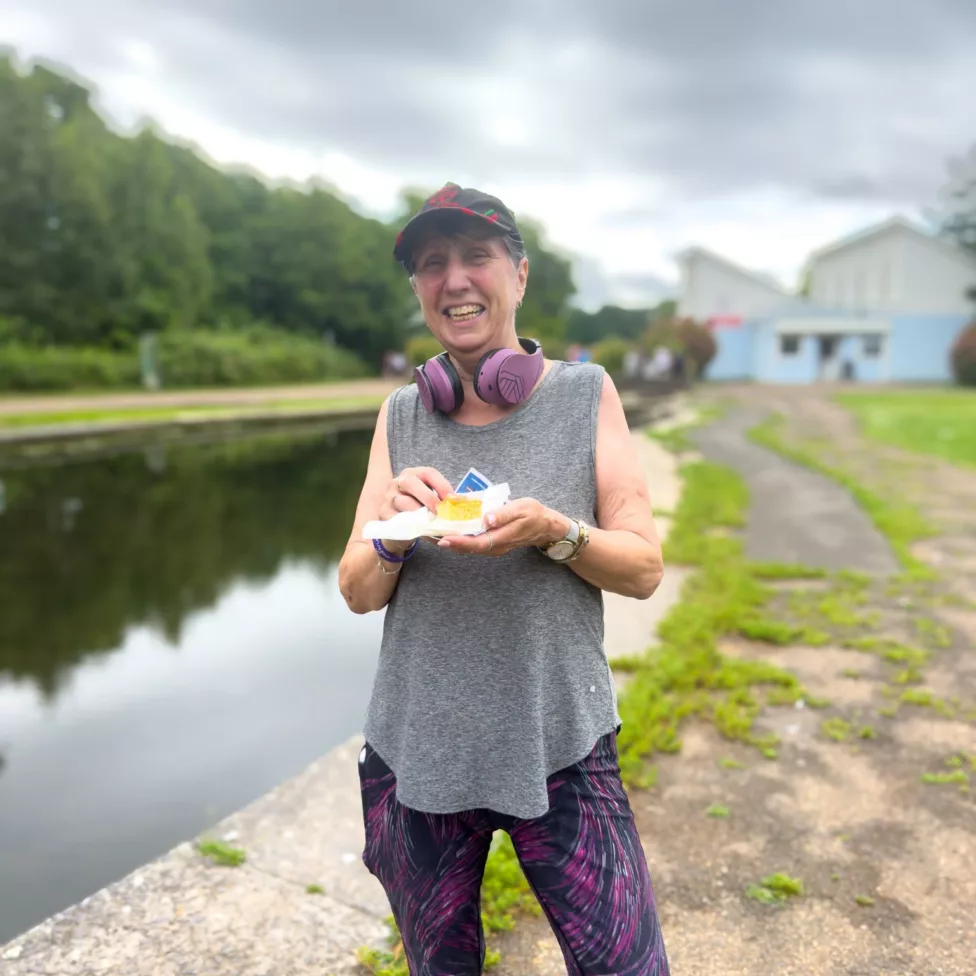 a woman in running clothes eating a cake by a pond