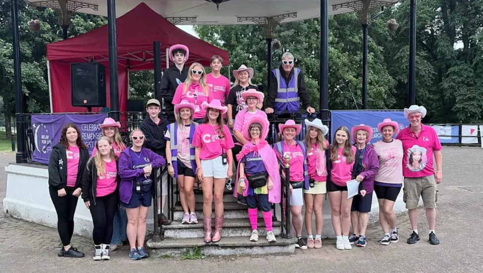a team of men and women- many in pink clothes stood by a bandstand