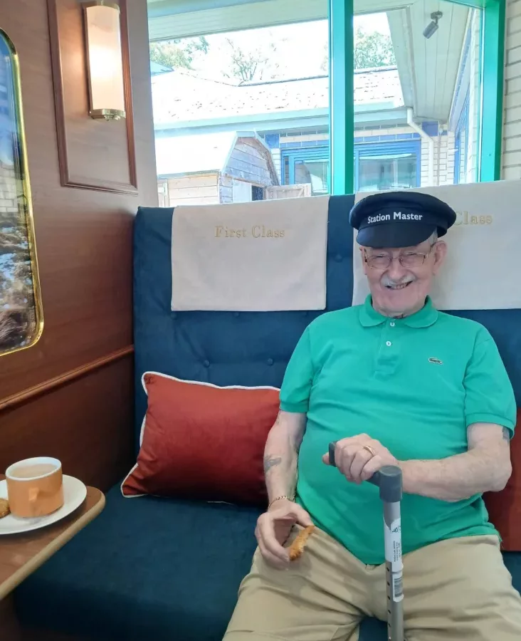 a photo of an older man in a train conductor hat sat in a train seat