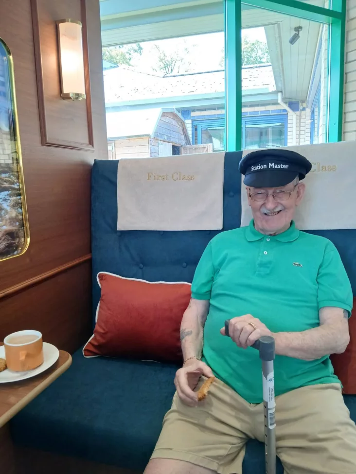 a photo of an older man in a train conductor hat sat in a train seat