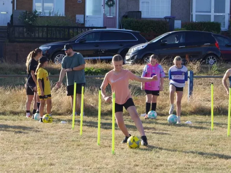 a girl dribbling a football through poles