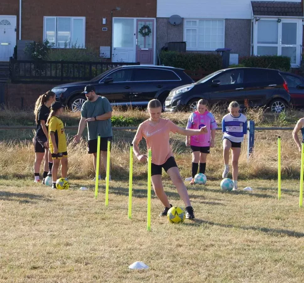 a girl dribbling a football through poles