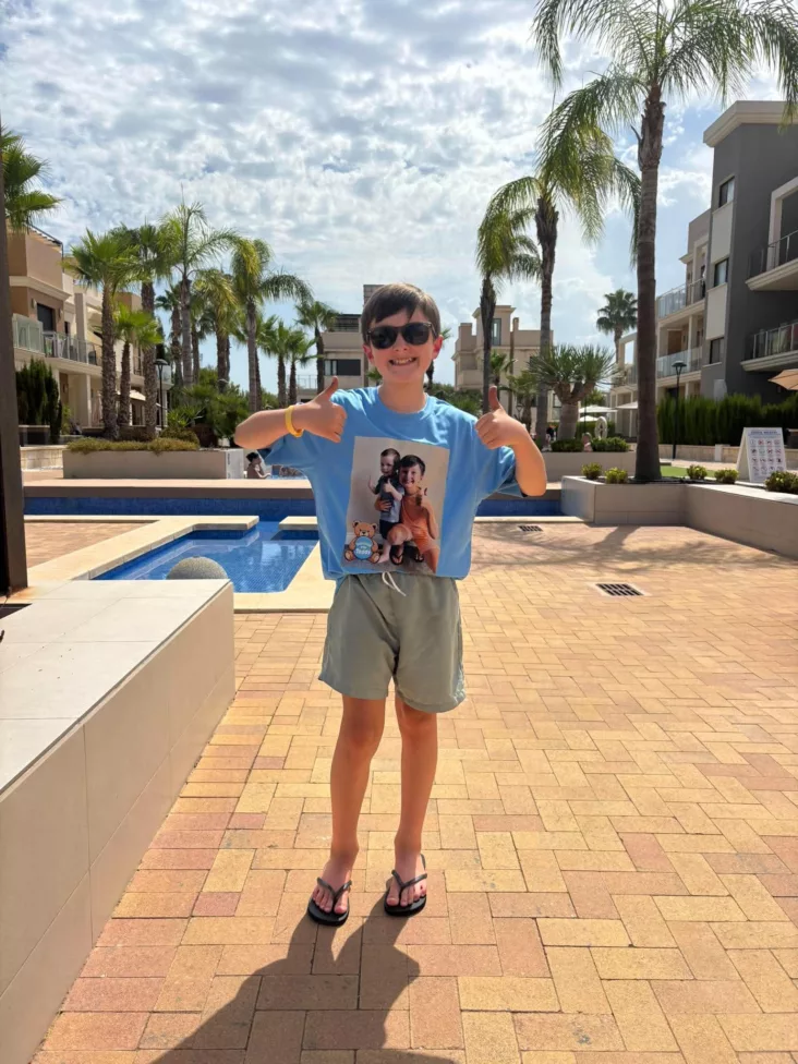 a young boy stood by a pool in the sun