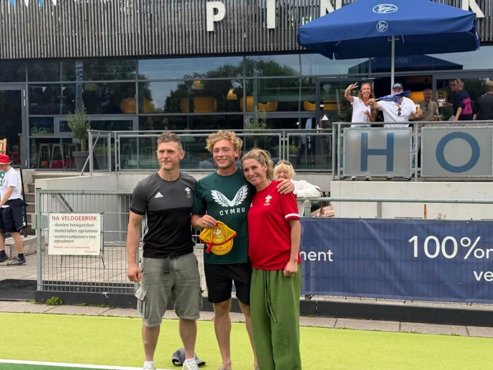 a man and woman with their son holding a red wales cap on a pitch