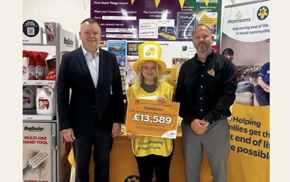 two men and a women with a daffodil hat on holding a cheque