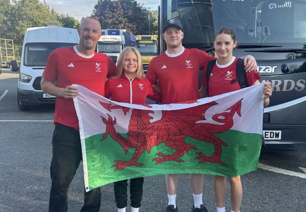 two men and two women hold a wales flag stood in front of a bus